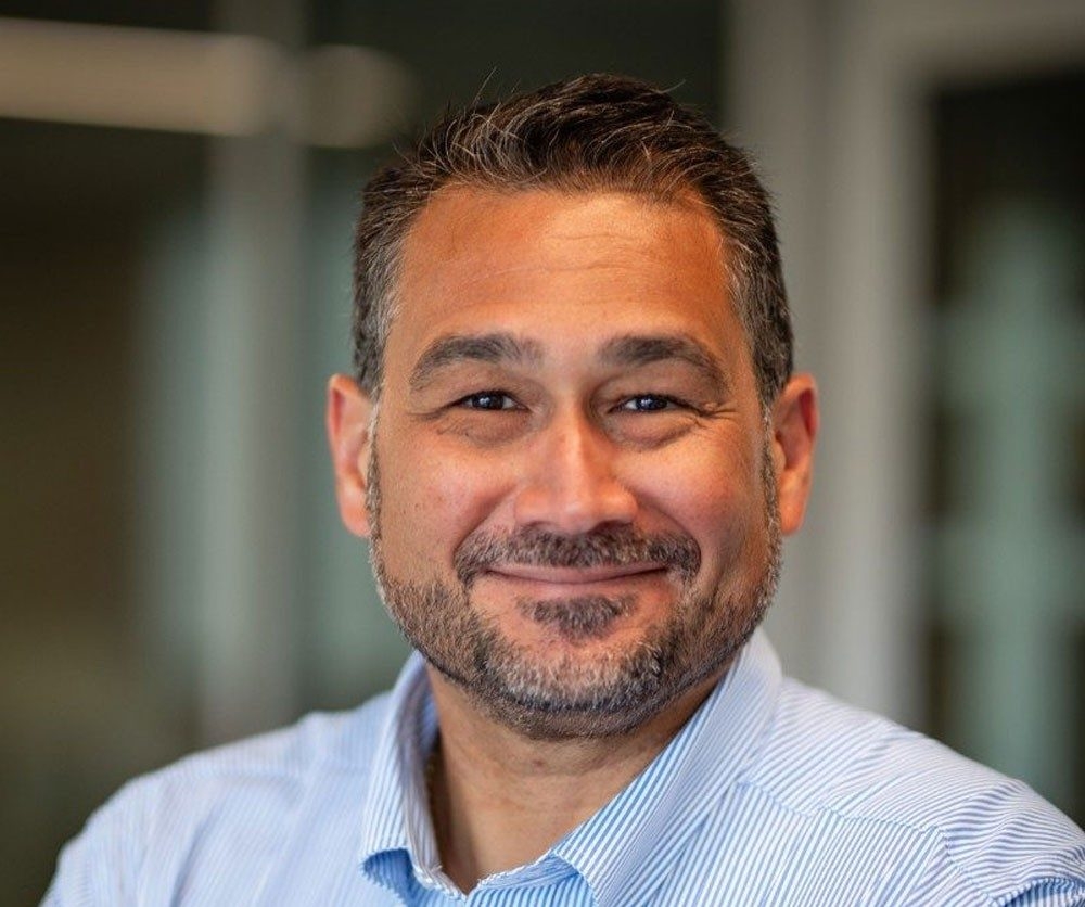 Miguel Perez Headshot of a gentleman with dark hair, beard, wearing a blue shirt