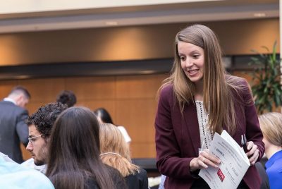 A BEAM graduate student holding a program prepares to take her seat at a conference presentation