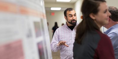 A BEAM graduate student explains his research findings to several onlookers during a presentation