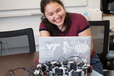 A BEAM undergrad laughs as she works at her laptop, modifying the programming of her robot.